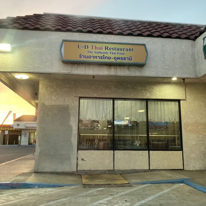 Exterior of U-D Thai Restaurant with its sign, large windows, and a parking lot at sunset.