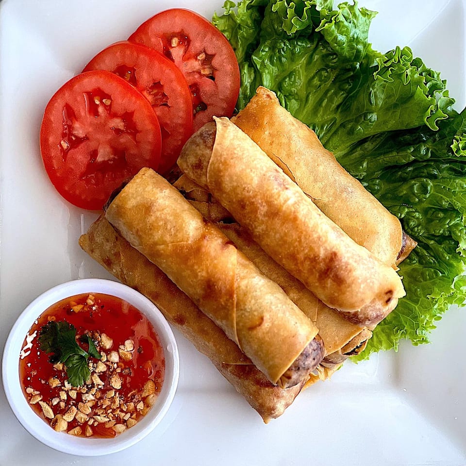 Crispy Thai spring rolls with fresh lettuce, sliced tomatoes, and a sweet chili dipping sauce.