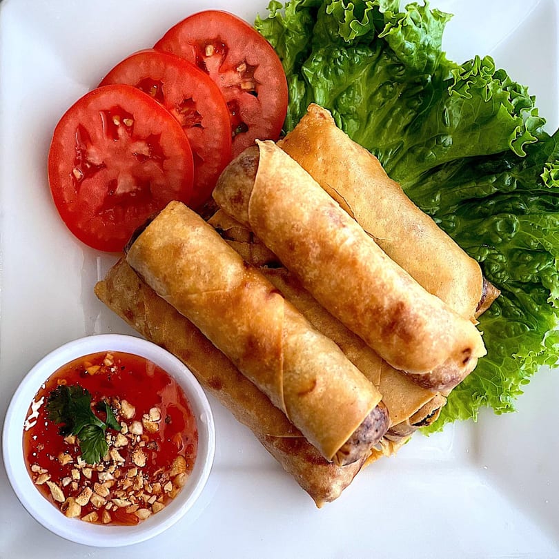 Crispy Thai spring rolls with fresh lettuce, sliced tomatoes, and a sweet chili dipping sauce.
