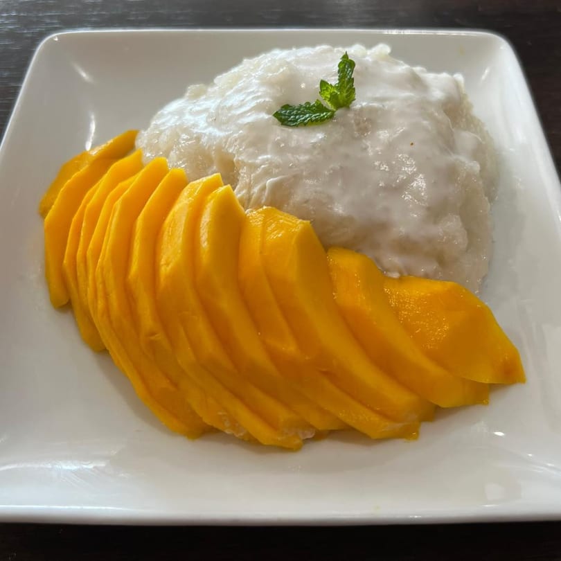Mango sticky rice with sliced mangoes and a mint garnish on a white plate.