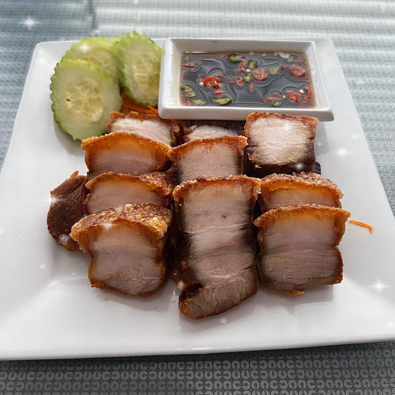 Crispy pork belly slices with a side of cucumber and a dark dipping sauce on a white plate.