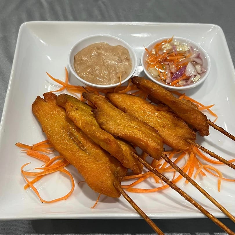 Golden chicken satay skewers with peanut sauce and a pickled vegetable relish on a white plate.
